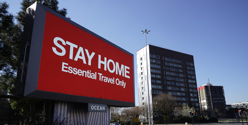 A digital board displays red background with white text that reads "STAY HOME" on the top and "Essential Travel Only" on the bottom — first opinion coverage from STAT