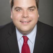 Headshot photograph of Adam Wright, a man smiling and looking at camera
